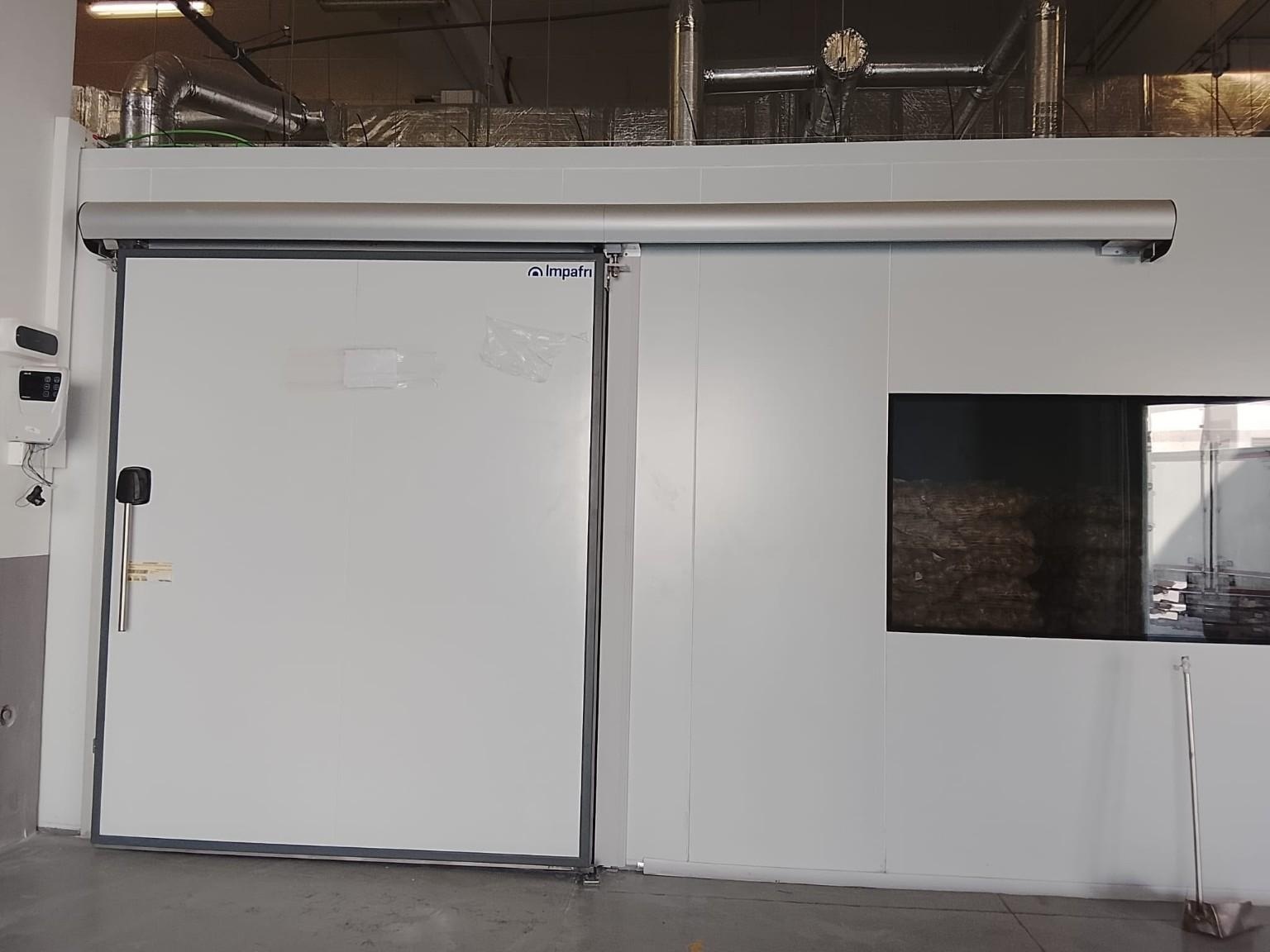 Porta corredissa sanitària de grans dimensions integrada en panell sandvitx